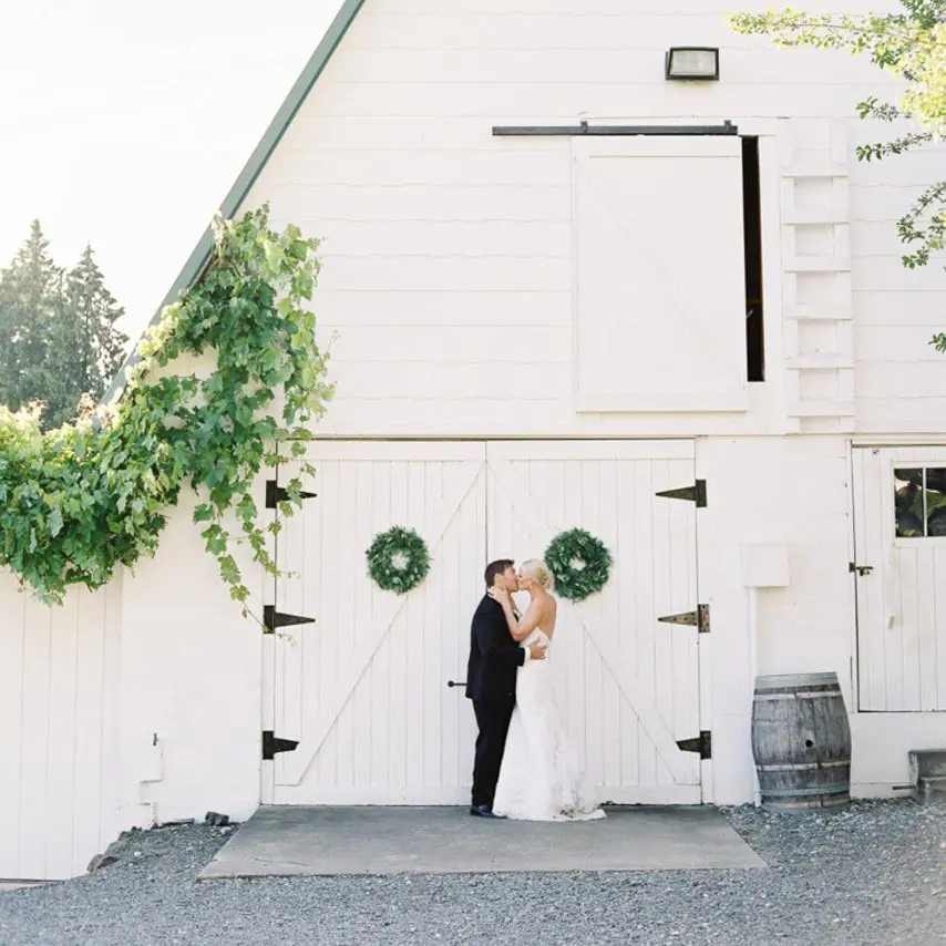 Bride and groom kissing in front of white barn | Lisa Dupar Catering | Wedding & Event Catering in Seattle