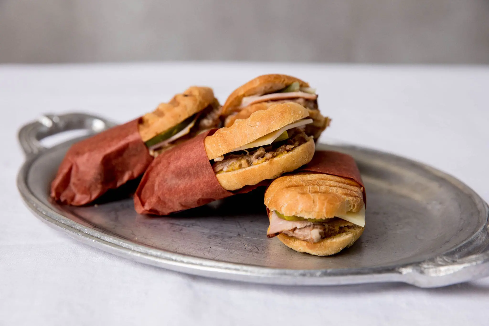 Seattle Catering Three wrapped sandwiches featuring meat, cheese, and pickles are elegantly presented on a silver tray, perfect for catering menus.