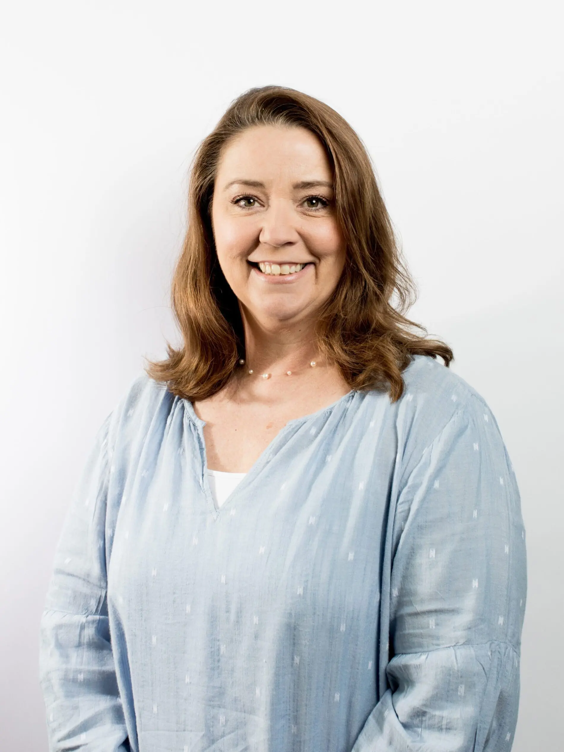 Seattle Catering A woman with shoulder-length brown hair, wearing a light blue blouse, smiles at the camera against a plain white background.