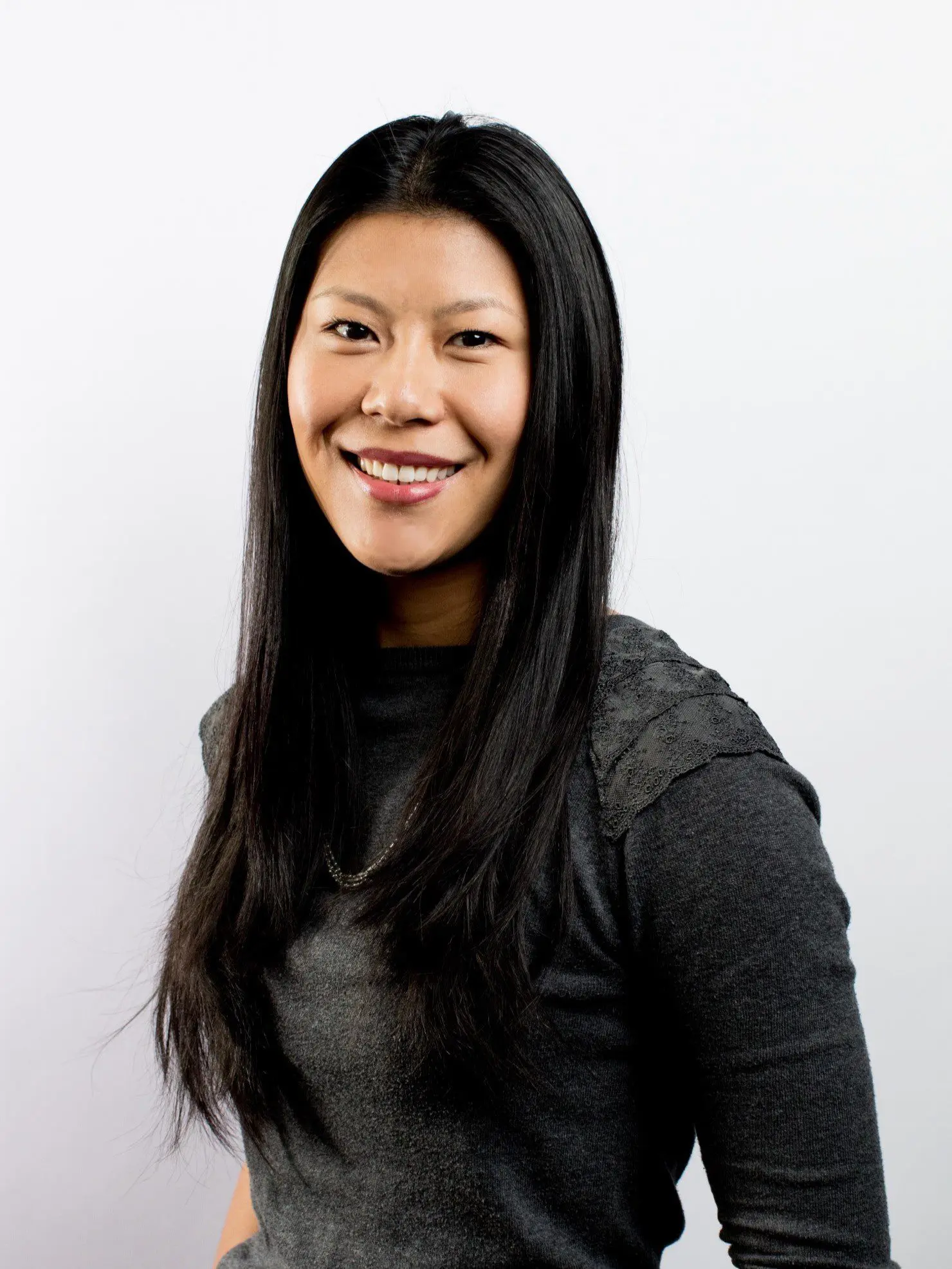 Seattle Catering A woman with long black hair, wearing a dark gray long-sleeve shirt, smiles in front of a plain light background.