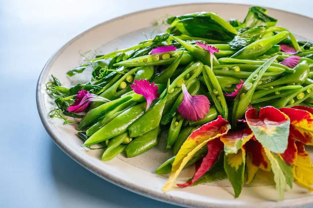 Seattle Catering Plate of fresh green sugar snap peas garnished with vibrant pink petals and colorful leaves.