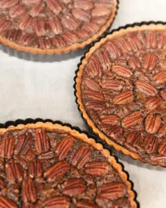 Seattle Catering Three pecan pies with crispy crusts and neatly arranged pecan halves on a light surface.