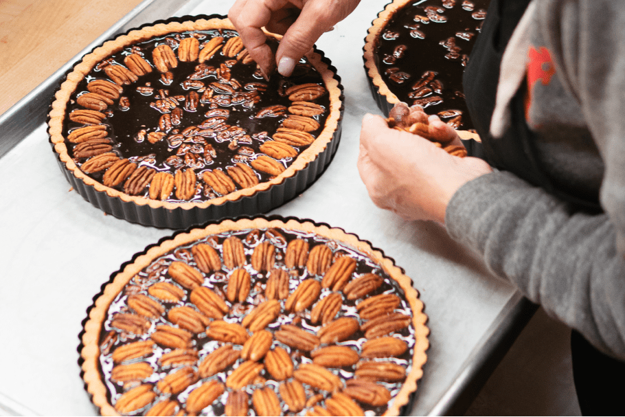 Seattle Catering Person arranging pecans on chocolate tarts placed on a tray.