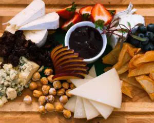 Seattle Catering A wooden board with various cheese slices, nuts, dried fruits, sliced fruit, strawberries, and a dish of dark jam in the center.