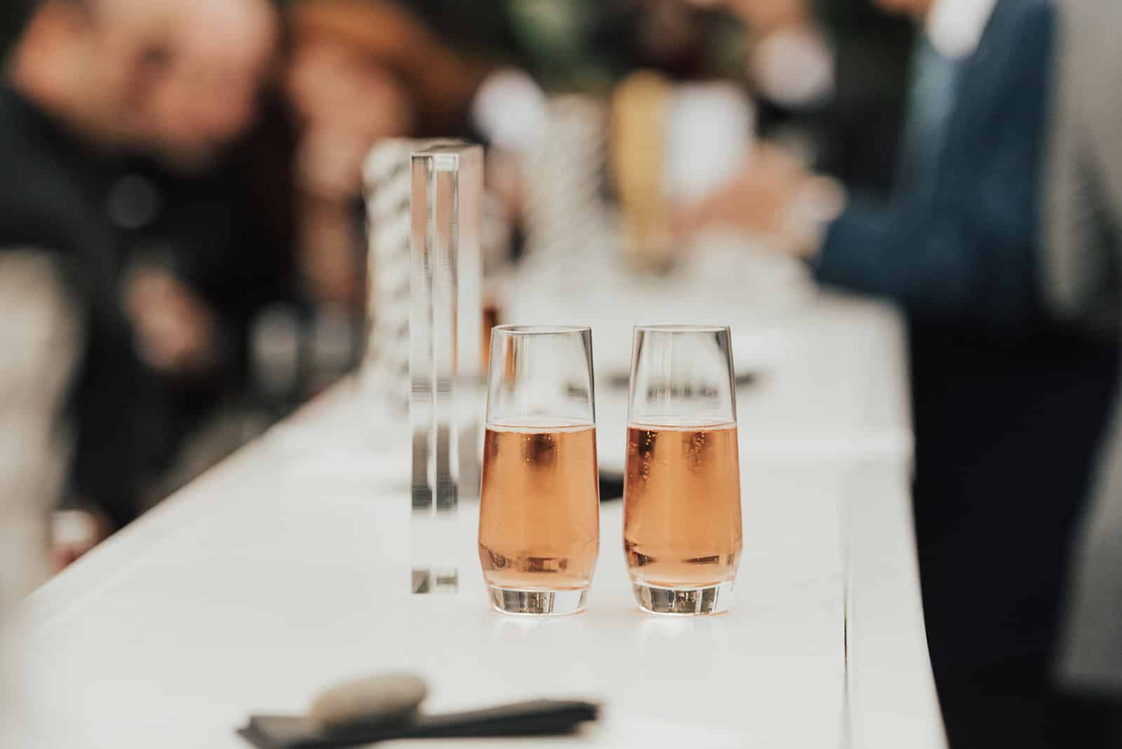 Two glasses filled with a pinkish beverage are placed on a white counter, capturing the elegant touch of wedding catering Seattle style, with people blurred in the background.
