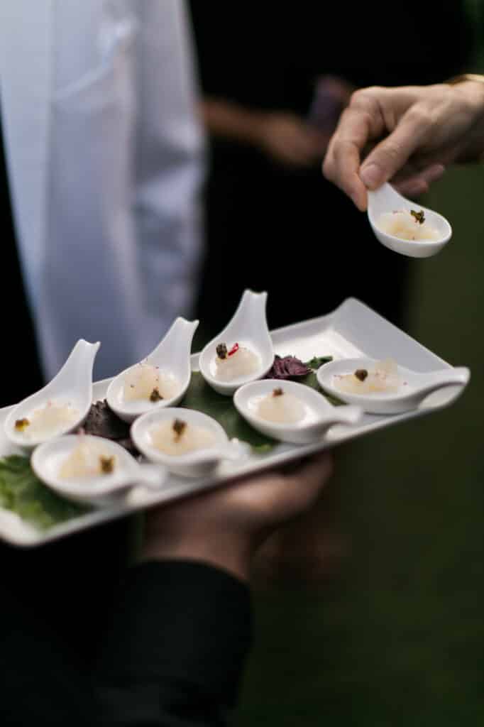A server presenting an individually portioned appetizer for a catered guest.