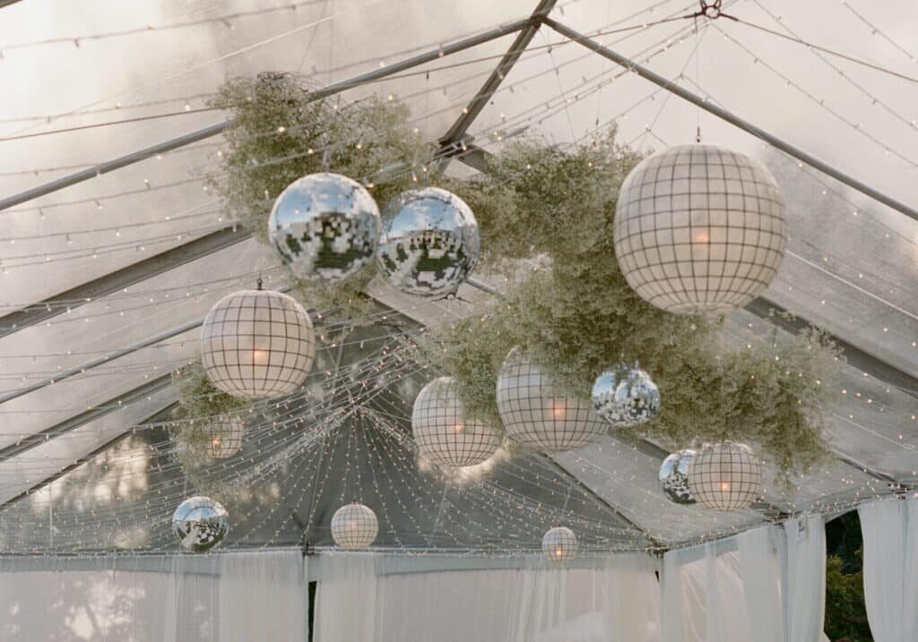 Clear tent ceiling decorated with hanging disco balls, round white lanterns, greenery, and string lights—an inspired setup often crafted by top event vendors in Seattle.