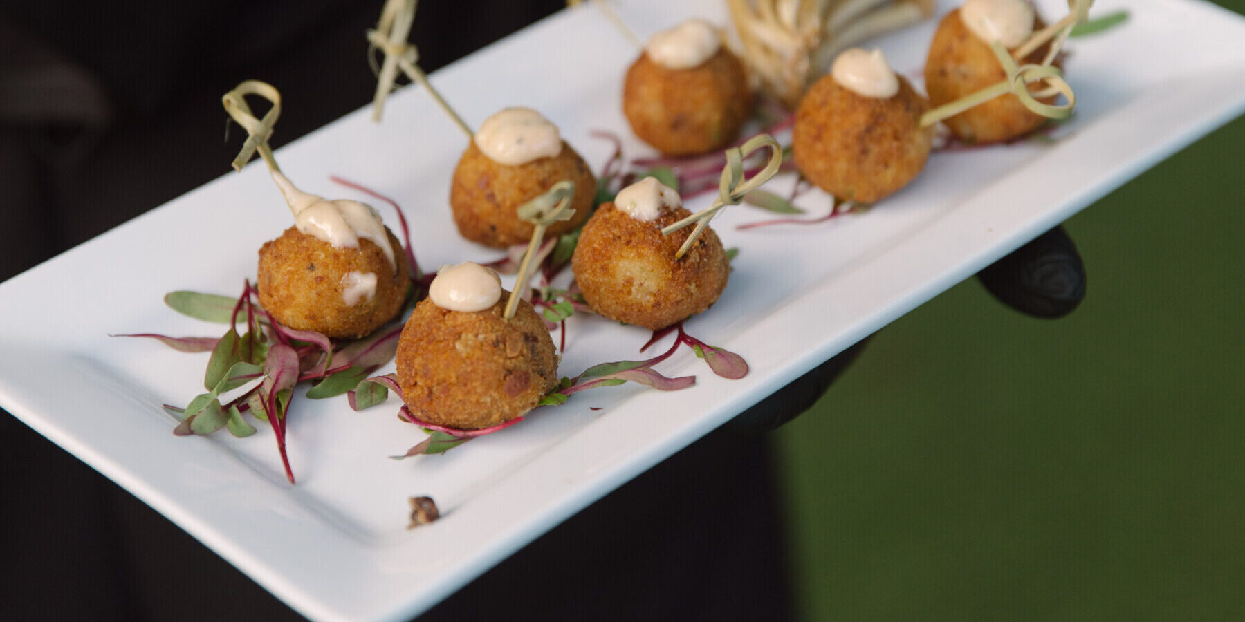 A rectangular white plate with small breaded appetizers on skewers, topped with a dollop of sauce and served on a bed of microgreens—an elegant bite perfect for Corporate Catering Seattle events.