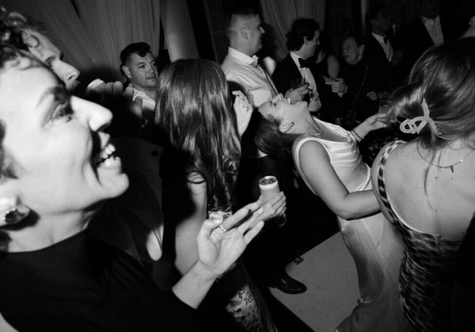 A group of people dressed formally laugh and dance at a lively indoor event catered by top Catering Services in Seattle, with one woman in a white dress tilting her head back in joy.