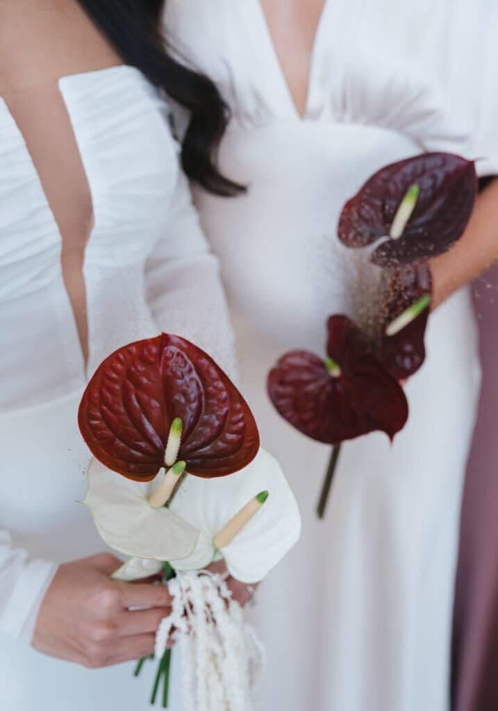 Two people in white dresses holding bouquets of white and dark red anthurium flowers, shown from the shoulders down—an elegant moment curated by top event vendors in Seattle.
